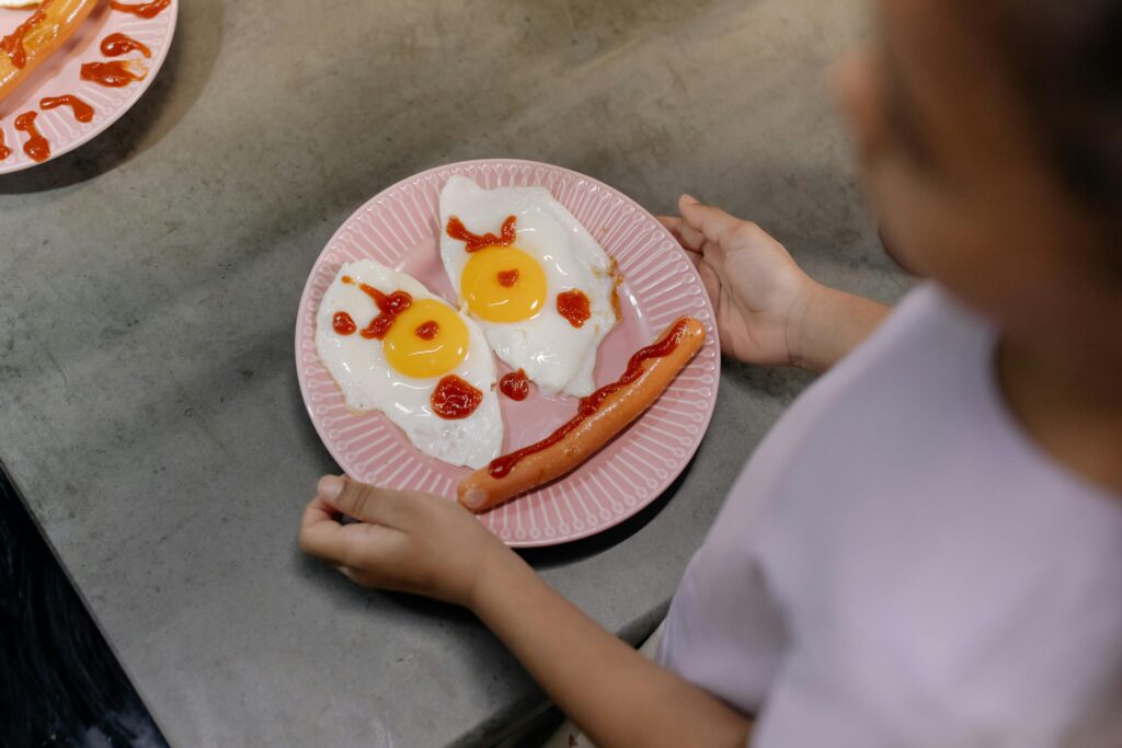 Playful breakfast setup featuring sunny-side-up eggs and sausage arranged like a smiling face on a pink plate.